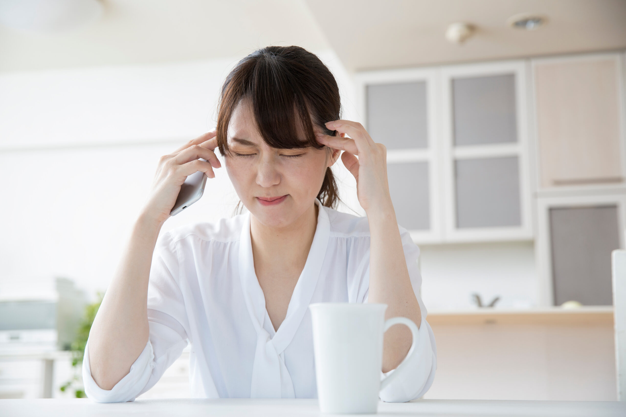 頭痛に悩む女性がこめかみに手を当ててつらそうにしている様子|天気頭痛や薬物乱用頭痛、漢方による対策を解説するコラム用イメージ