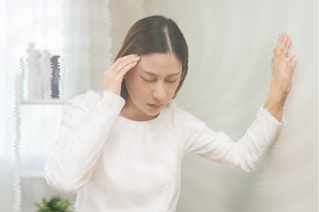 めまいでふらつき、壁に手をついてこめかみを抑える女性。視界がぼやけている様子